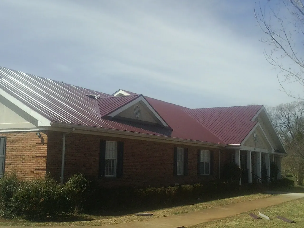 Red metal roof with gabled entries on a long brick building, from a Hail Damage Roof Repair job in Harrison City