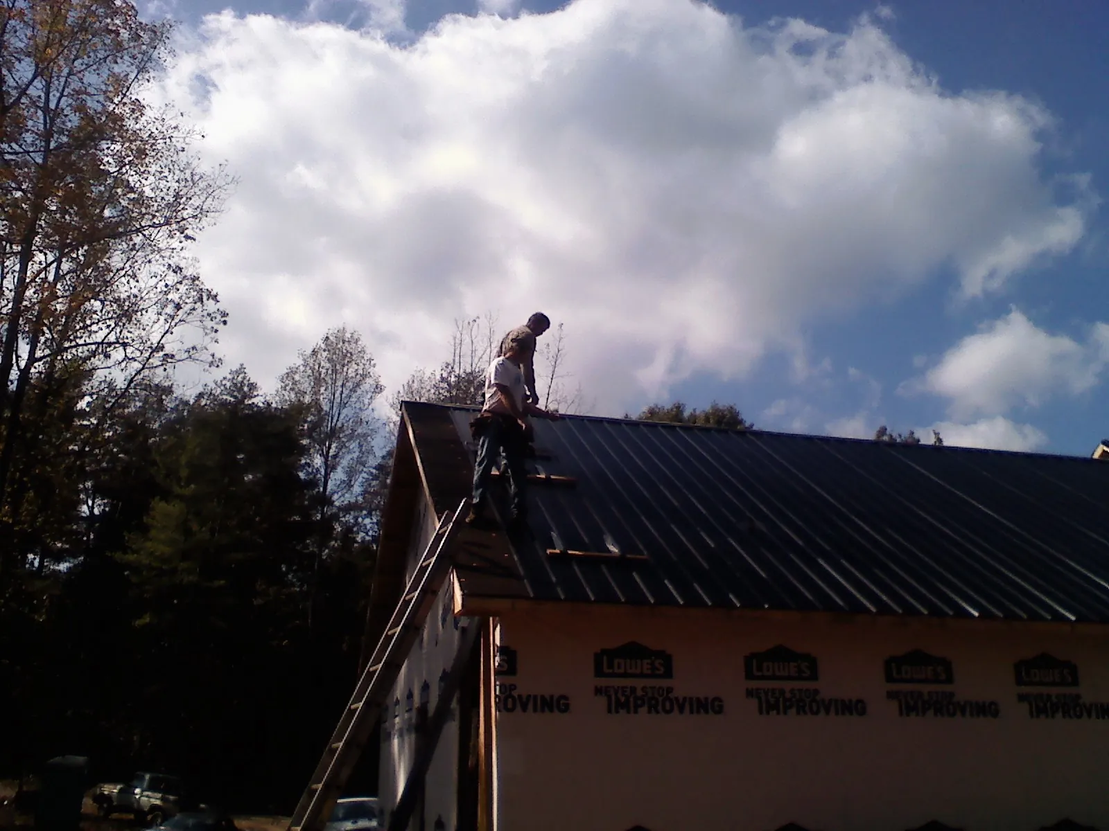 Roofer fastening dark metal panels high against a cloudy sky, from a Roof Inspection job in Harrison City