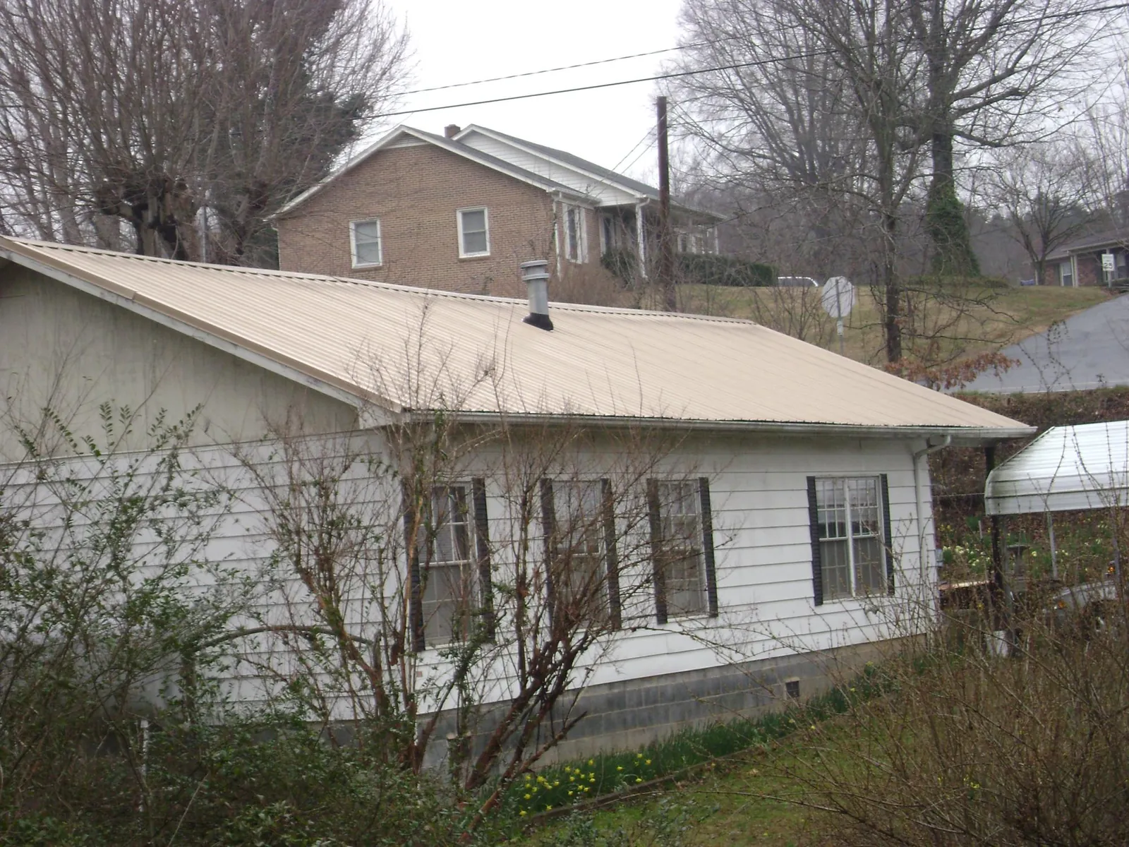 Tan metal roof on a white sided house set into a hillside — Commercial Roofing by Roofing Brothers in Harrison City